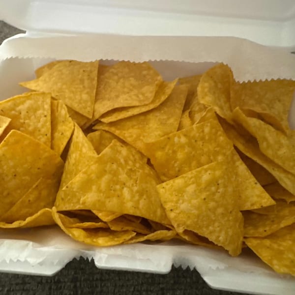 A white takeout container filled with a generous serving of crispy, golden tortilla chips from Elena's Taco Shop.