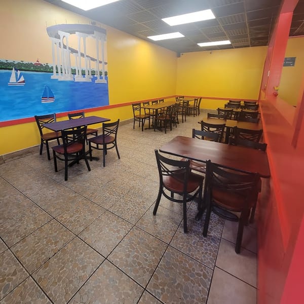 Elena's Taco Shop dining area with yellow walls, dark tables, chairs, and a mural of a bridge over water.