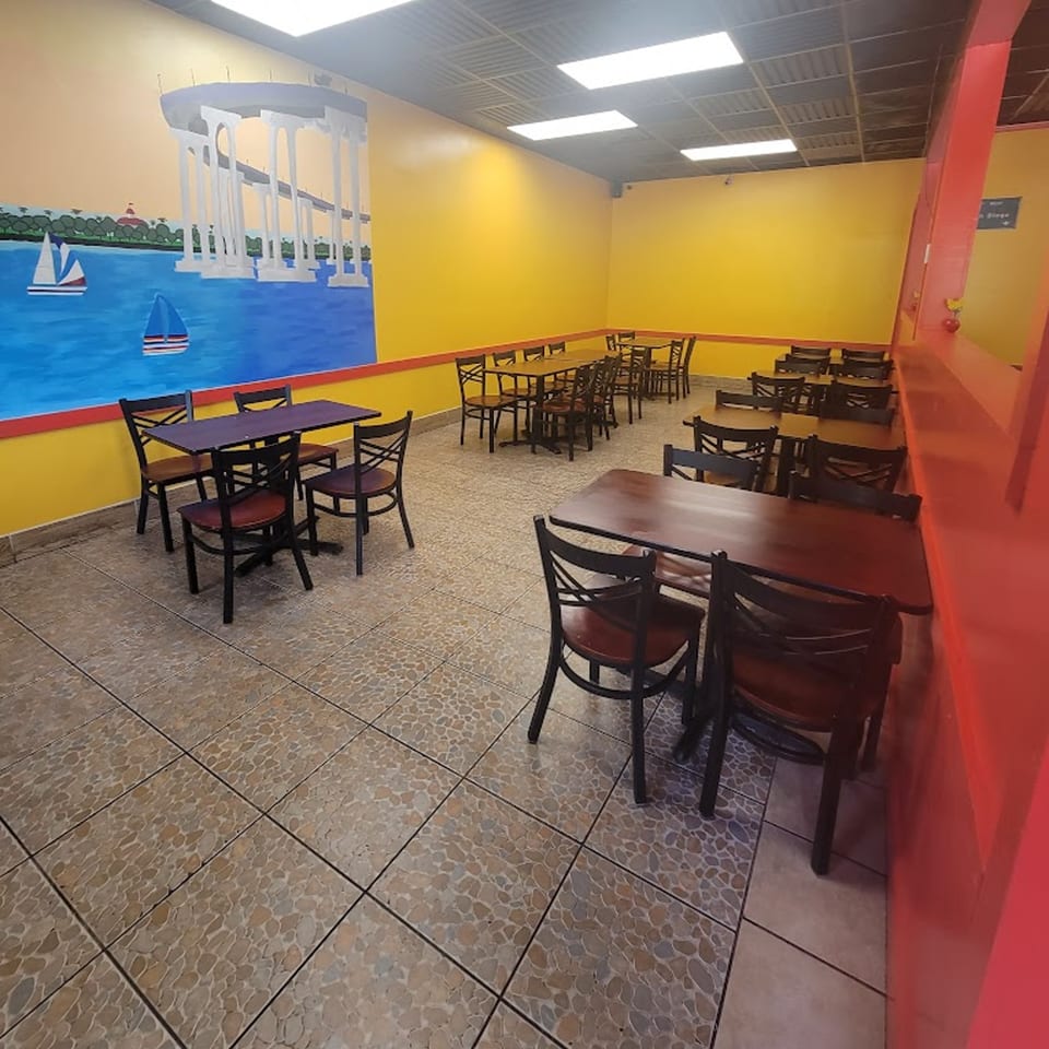 Elena's Taco Shop dining area with yellow walls, dark tables, chairs, and a mural of a bridge over water.
