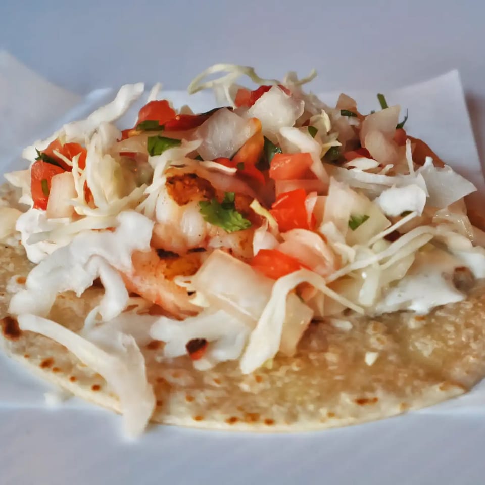 A shrimp taco from Elena's Taco Shop, topped with cabbage, pico de gallo, and crema.