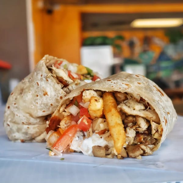 Two Elena's Taco Shop burritos, one cut open to show chicken, fries, tomatoes, and sauce.
