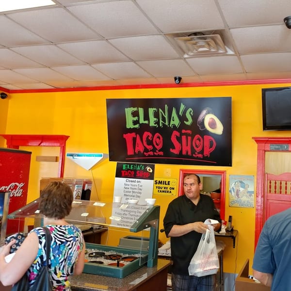Elena's Taco Shop interior with a customer at the counter and an employee holding a takeout bag.