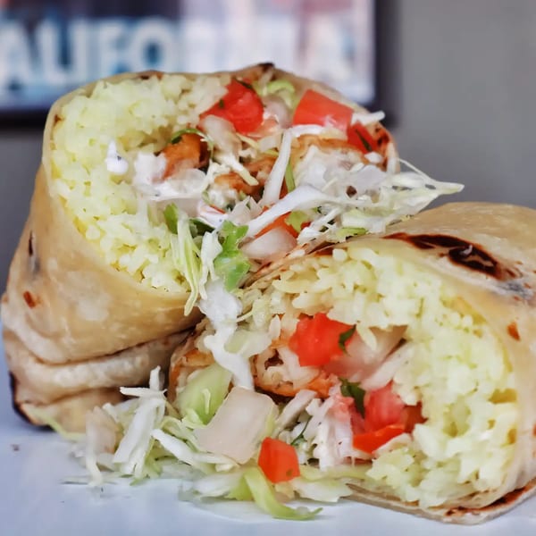 A large Elena's Taco Shop burrito, cut in half, revealing rice, chicken, lettuce, and tomatoes.