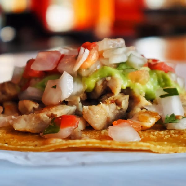 A close-up of a chicken taco from Elena's Taco Shop, topped with diced onions, tomatoes, and guacamole.