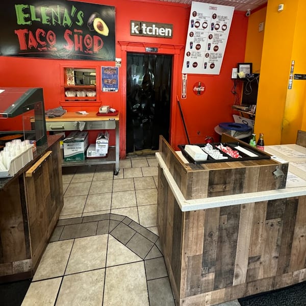 Interior of Elena's Taco Shop with red walls, a kitchen entrance, and a counter with condiments.