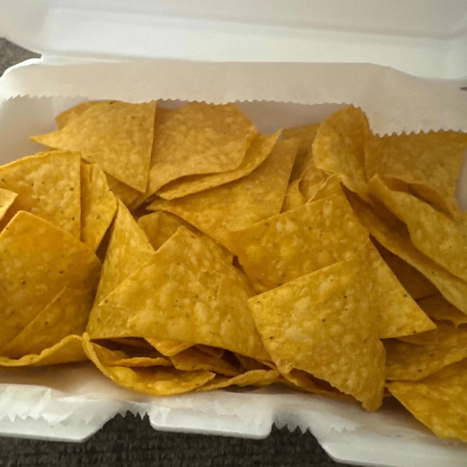 A white takeout container filled with a large serving of crispy, golden tortilla chips.