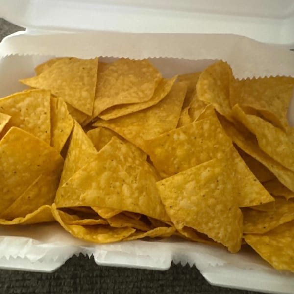 A white takeout container filled with a generous serving of golden, crispy tortilla chips from Elena's Taco Shop.