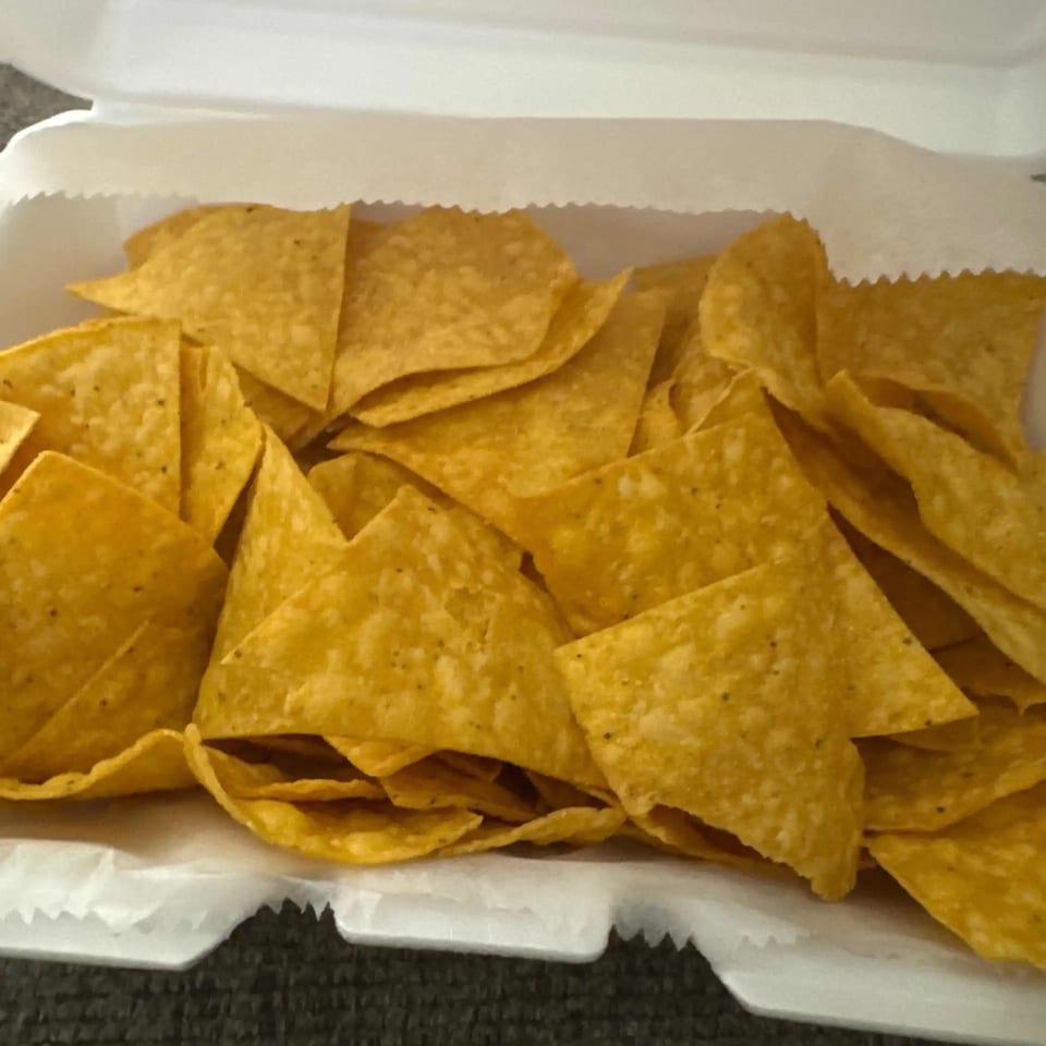 A white takeout container filled with a generous serving of golden, crispy tortilla chips from Elena's Taco Shop.